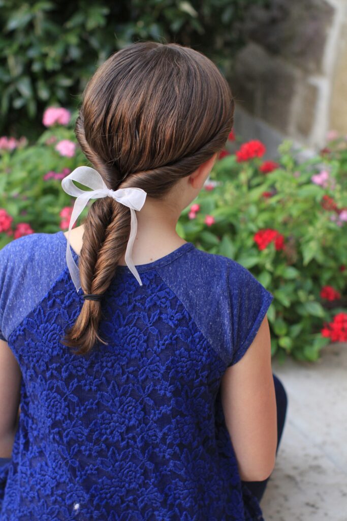 Back view of young girl standing outside and modeling “Double-twist" ponytail