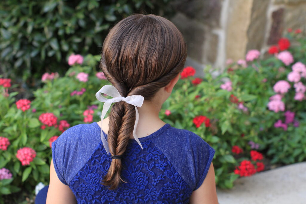 Back view of young girl standing outside and modeling “Double-twist" ponytail