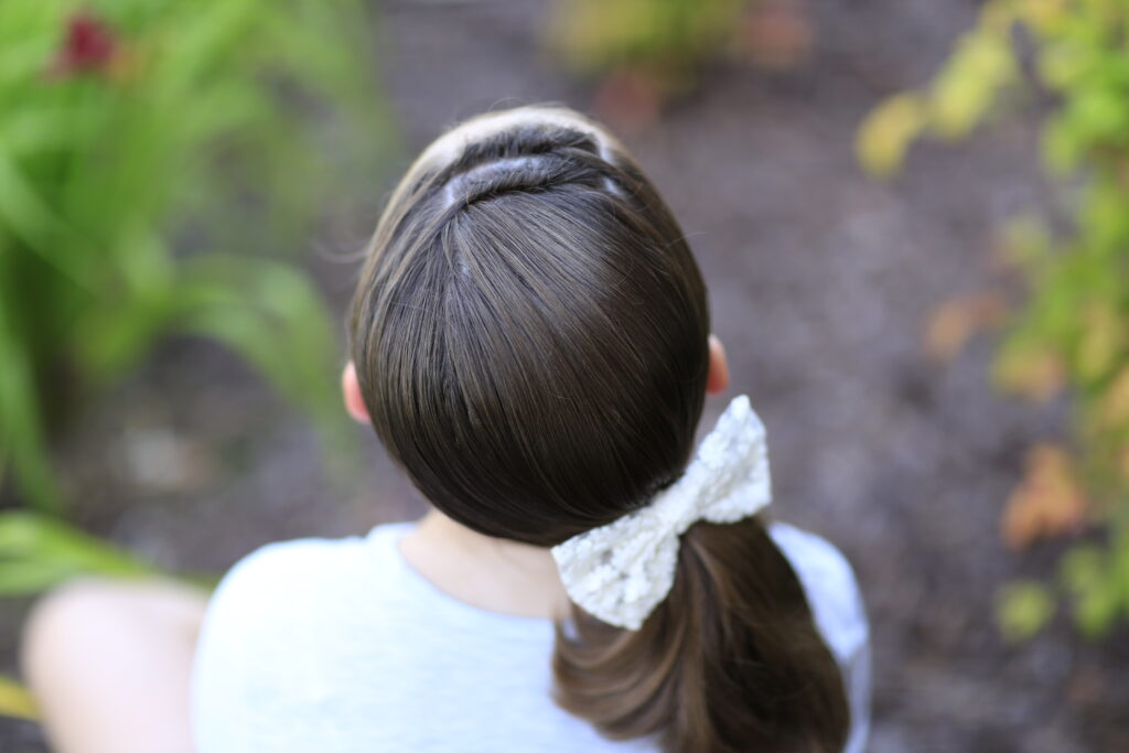 Back view of young girl outside modeling "Knots into Side Ponytail" hairstyle