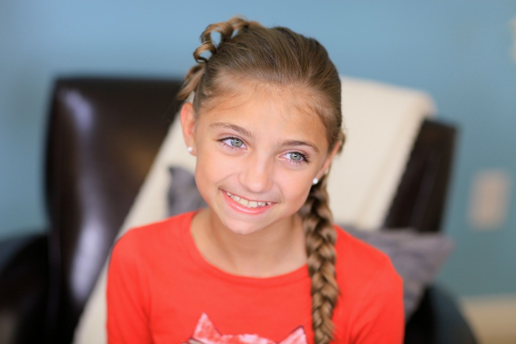 Portrait of young girl wearing a red shirt indoors modeling Diagonal Bow Braid | Popular Hairstyles