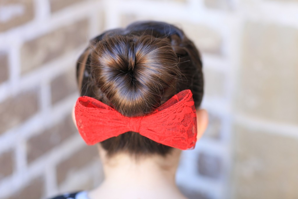 Young girl outside modeling "Love Bun" with a red bow in her hair | Valentine's Day Hairstyles