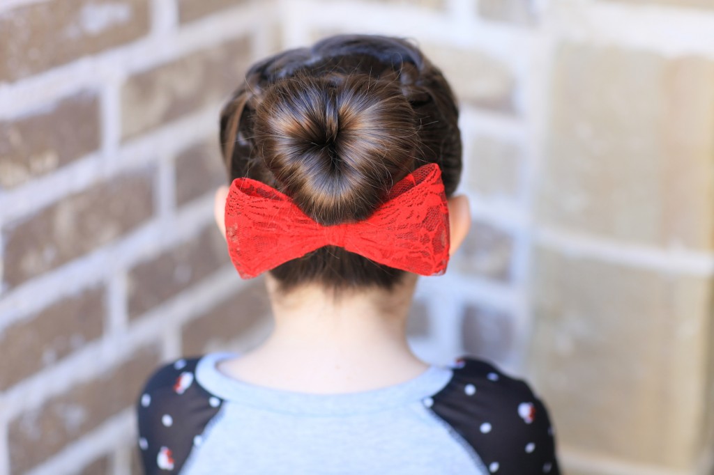 Young girl outside modeling "Love Bun" with a red bow in her hair | Valentine's Day Hairstyles