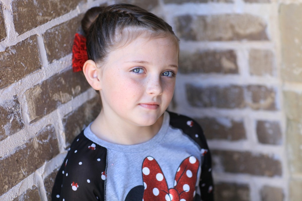 Portrait of young girl outside modeling "Love Bun" with a red bow in her hair | Valentine's Day Hairstyles