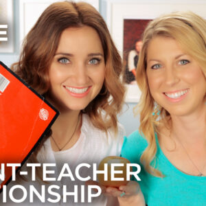 Two women posing together holding an apple and a notebook