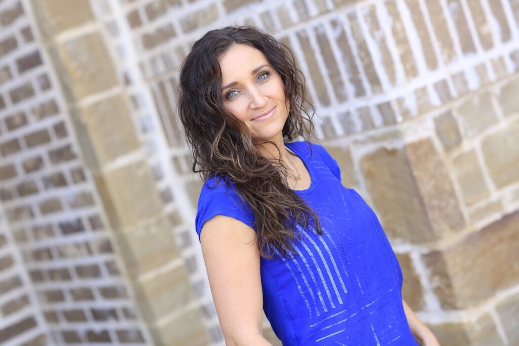 Woman with curly hair wearing a blue shirt outside in front of a brick background