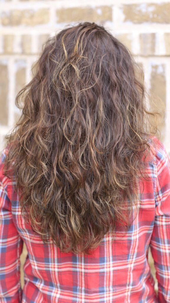 Woman with curly hair wearing a red plaid shirt standing outside in front of a brick background