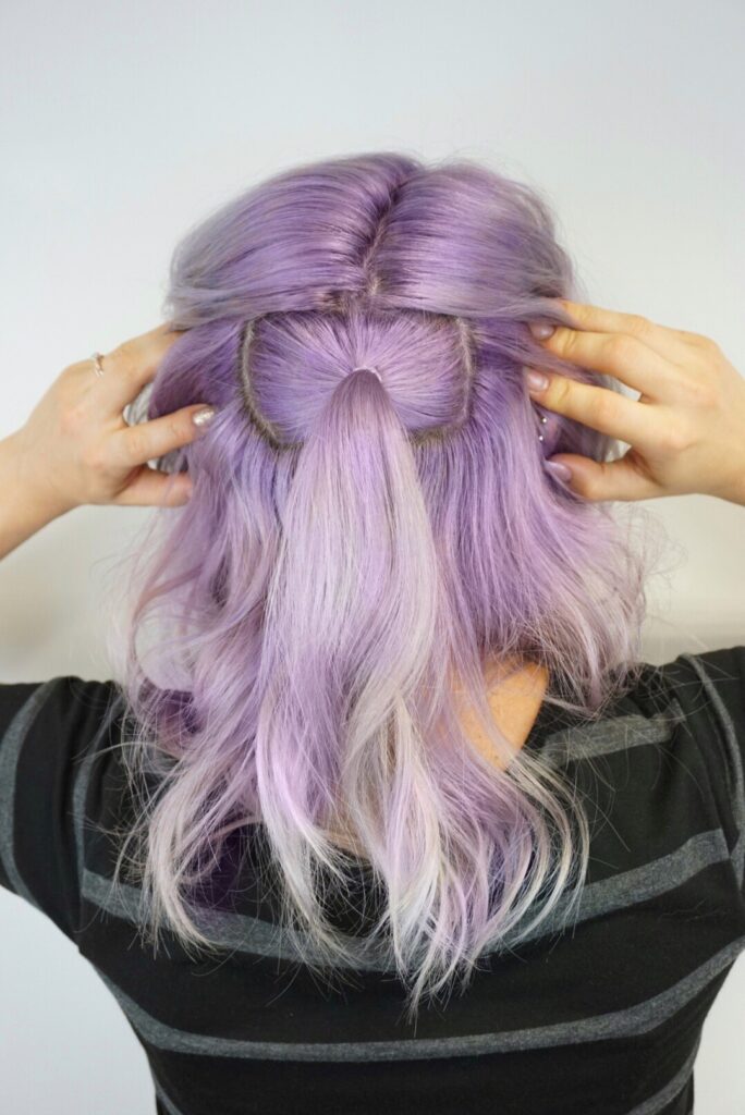 Girl holding her hair apart, displaying a smaller ponytail at her crown.