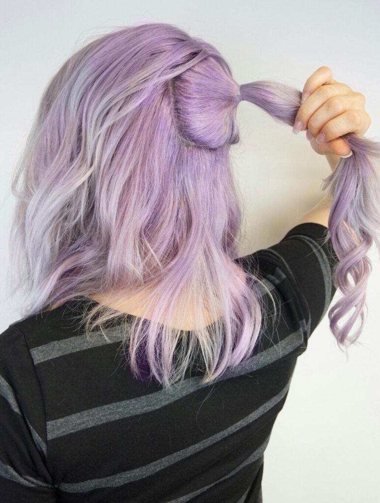 Girl standing in front of white background hold up a small ponytail in her hair.