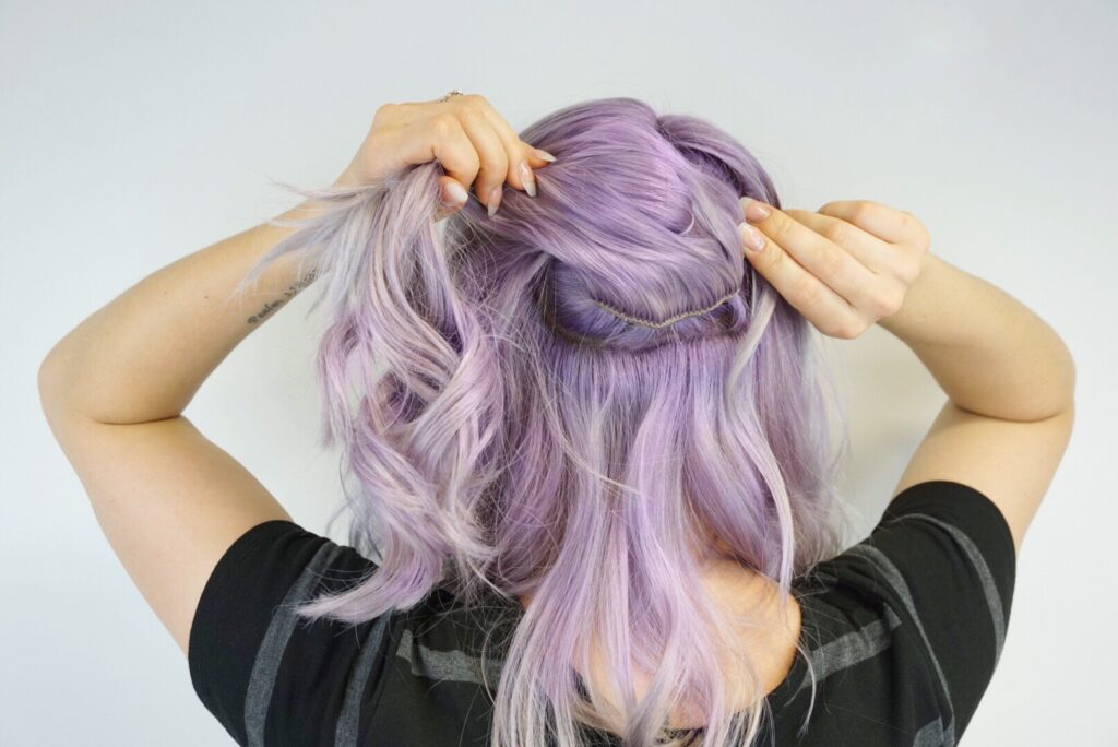 Back view of girl wrapping her hair into a hair tie to make a small ponytail while showing clip-in extension