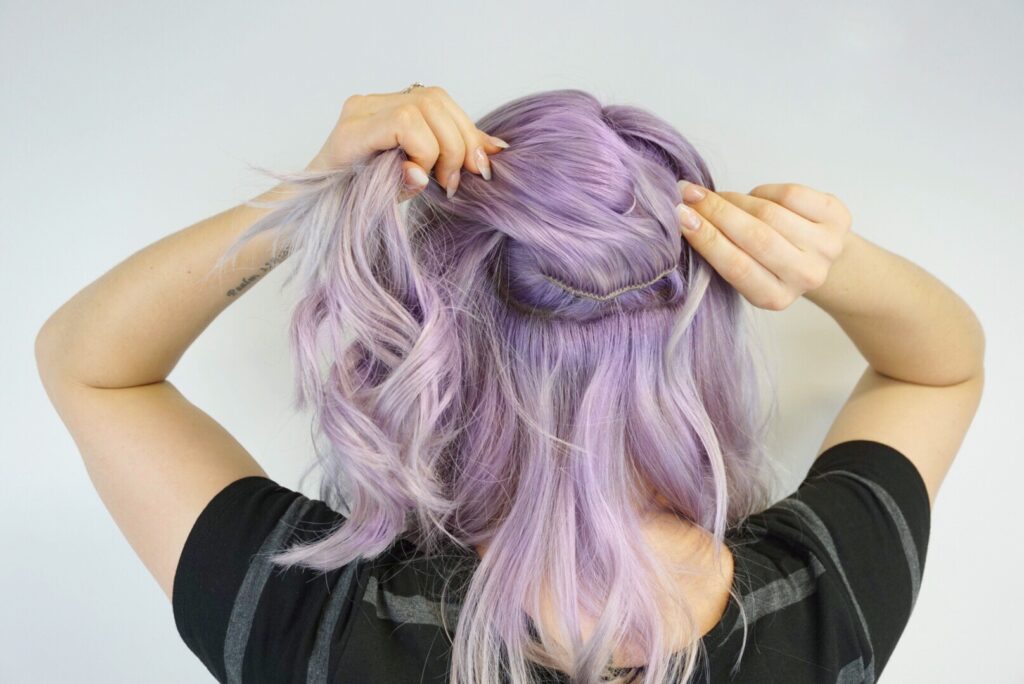 Back view of girl wrapping her hair into a hair tie to make a small ponytail while showing clip-in extension