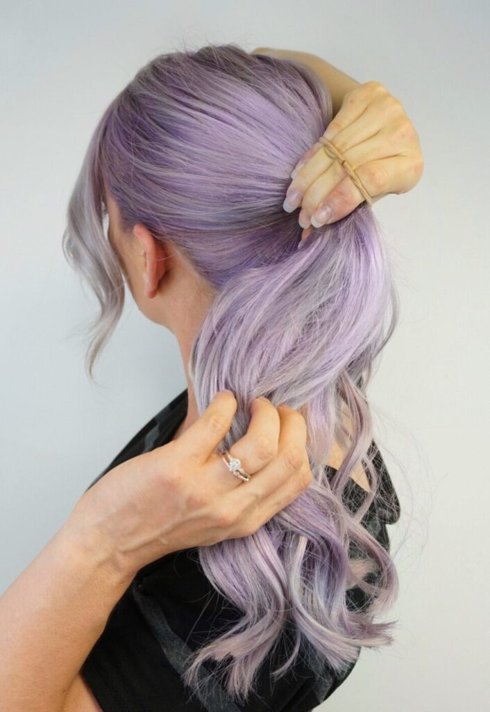 Side view of a girl putting hair into a nude hair tie to make a ponytail. 