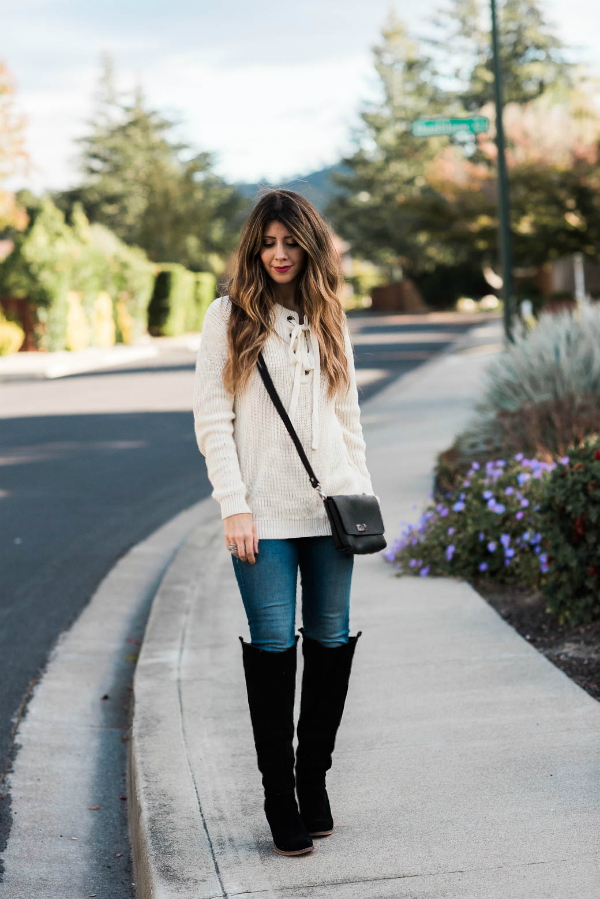 Woman outside wearing a white sweater, denim pants, black boots, and black crossbody bag