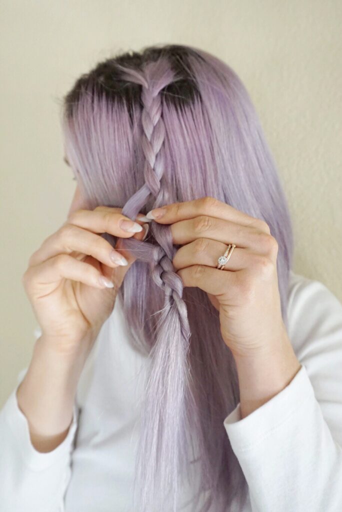 Woman wearing a white shirt braiding her lavender dyed hair 