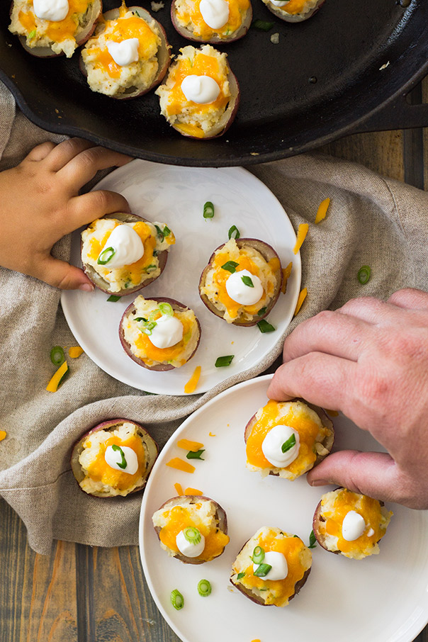 Father and child grabbing Twice Baked Potato Bites off white plates