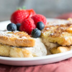 Eggnog French Toast with spiced cheesecake filling topped with strawberries, raspberries, and blueberries on a white plate