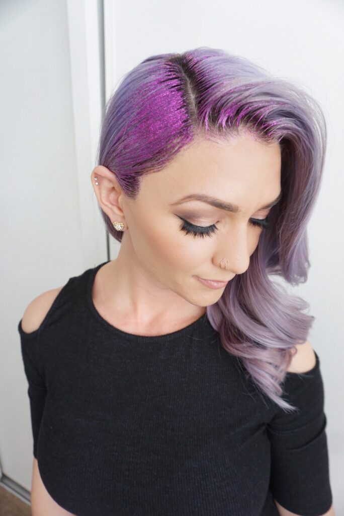 Side view of a young woman wearing a black shirt with purple hair and purple glitter