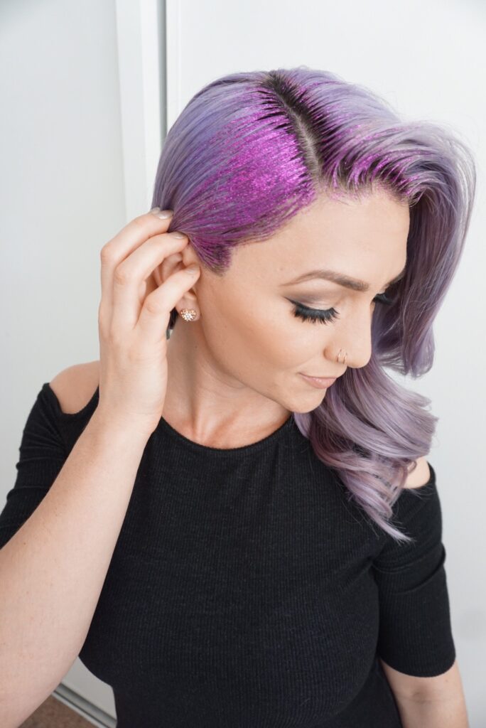 Side view of a young woman wearing a black shirt touching her purple hair and purple glitter gel