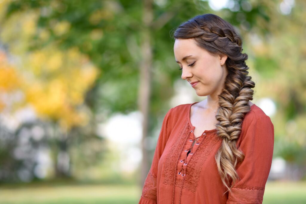 Side view of girl outside wearing an orange shirt modeling "Side Elastic Braid" hairstyle