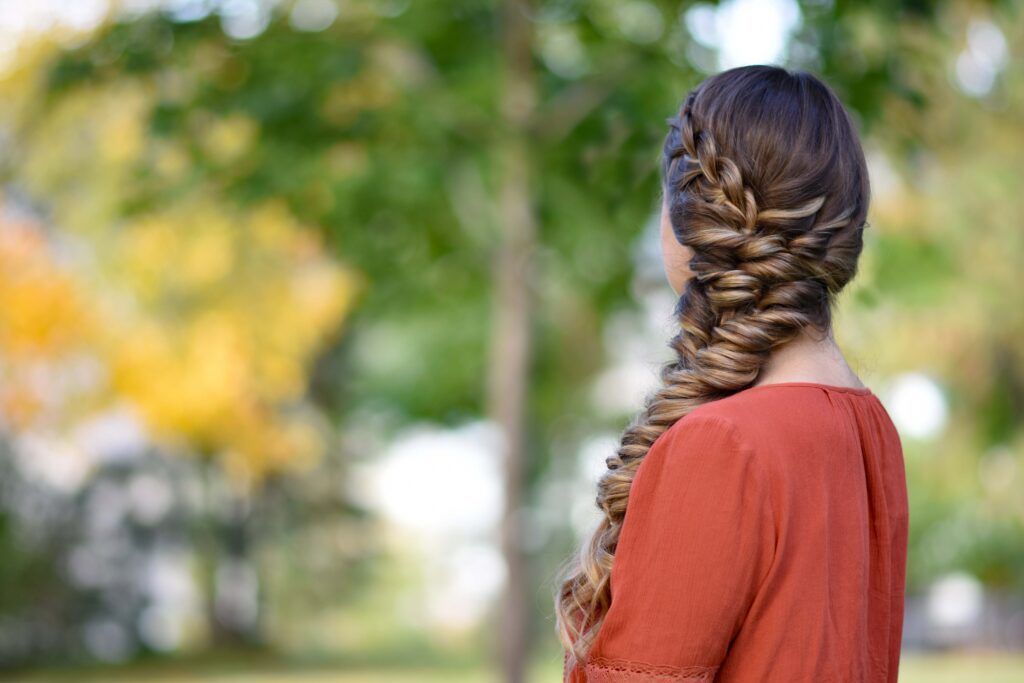 Side view of girl outside wearing an orange shirt modeling "Side Elastic Braid" hairstyle