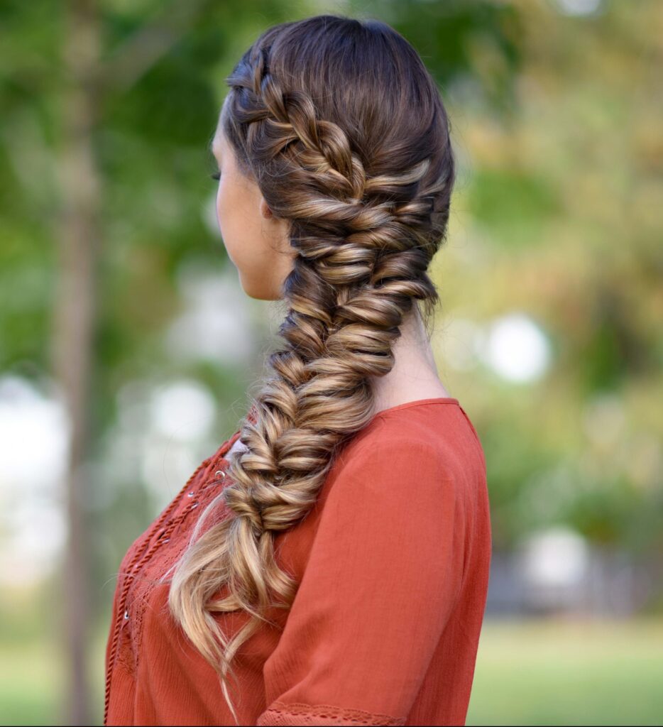 Side view of girl standing outside wearing an orange shirt modeling "Side Elastic Braid" hairstyle