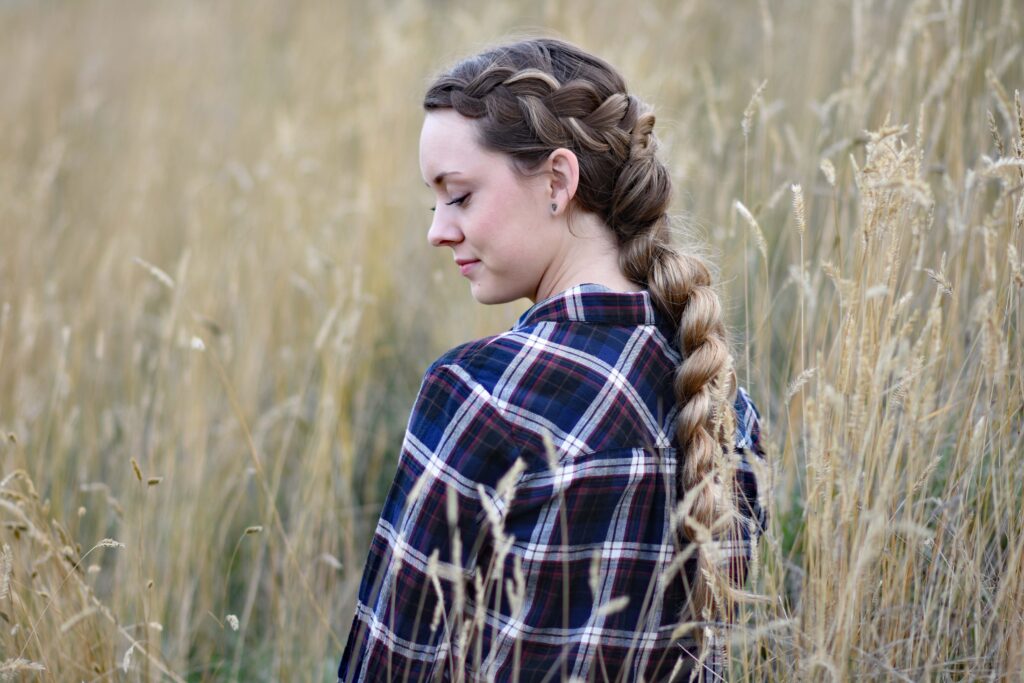 Side view of young girl in the meadow wearing blue plaid shirt modeling "Wrapped Pull-Thru Braid" hairstyle