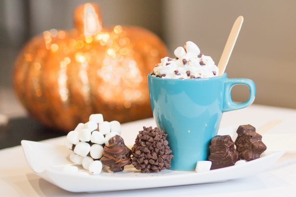 A blue coffee mug filled with hot cocoa and whipped cream with chocolate sprinkles surrounded by 'Hot Chocolate Pops'