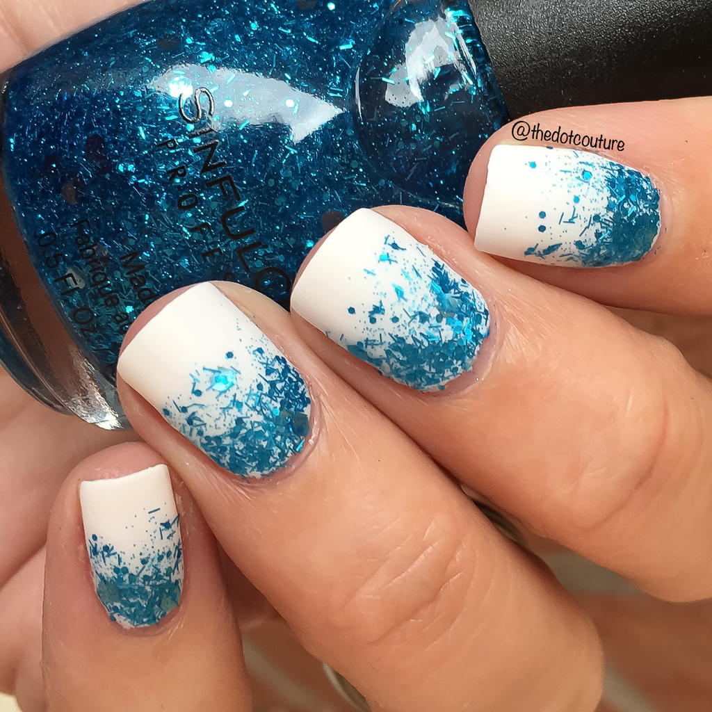 White painted nails with blue glitter holding a bottle of blue glitter nail polish