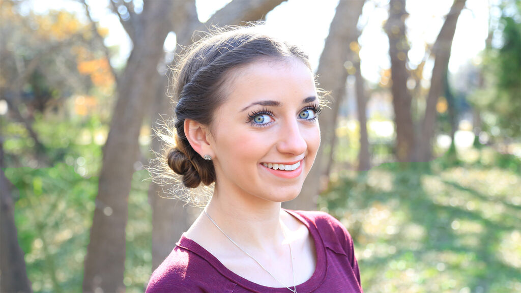 Portrait of a young girl smiling wearing a burgundy shirt, outside 