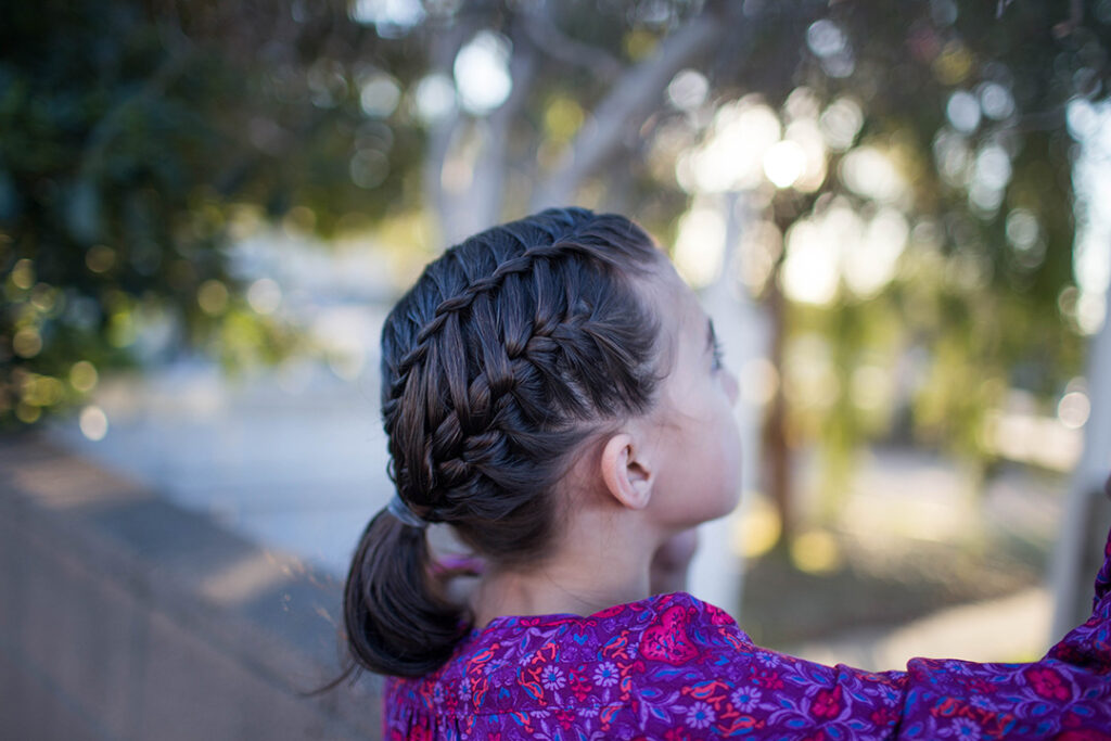 Side view of a young girl playing outside modeling "Gym Braid Combo" hairstyle