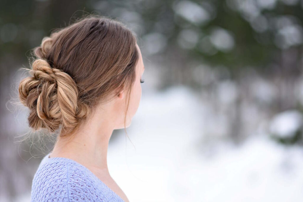 Side view of a girl in a purple shirt, standing outside modeling a "Stacked Fishtail Updo" hairstyle