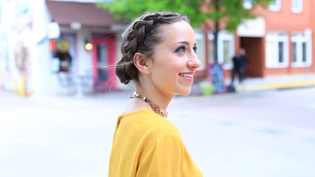 Profile of young girl smiling wearing a yellow shirt standing outside by a sidewalk