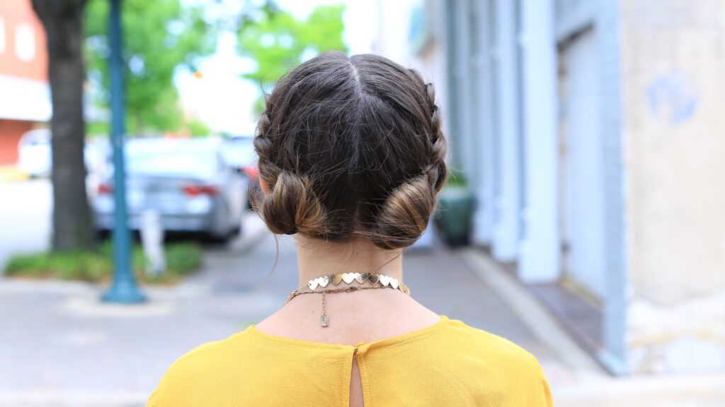 Back view of girl with a yellow shirt standing outside smiling modeling the "Double Dutch Buns" hairstyle