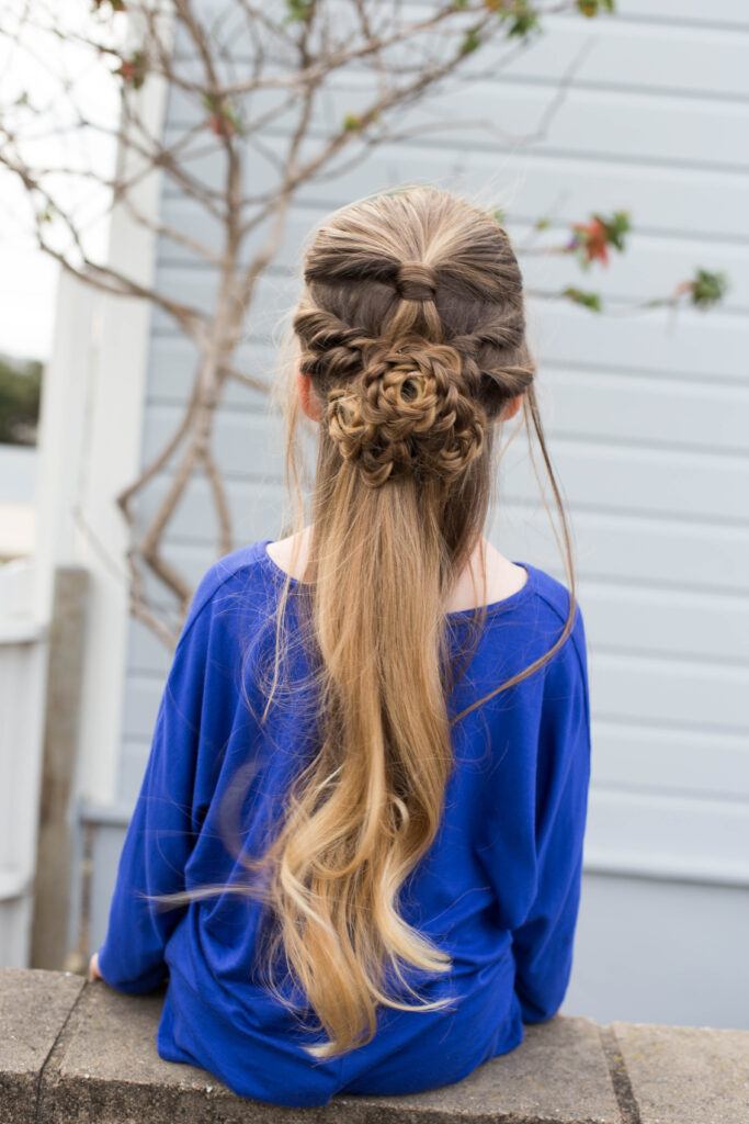 Back view of a little girl wearing a blue dress sitting outside modeling "Flower Half-Up" hairstyle