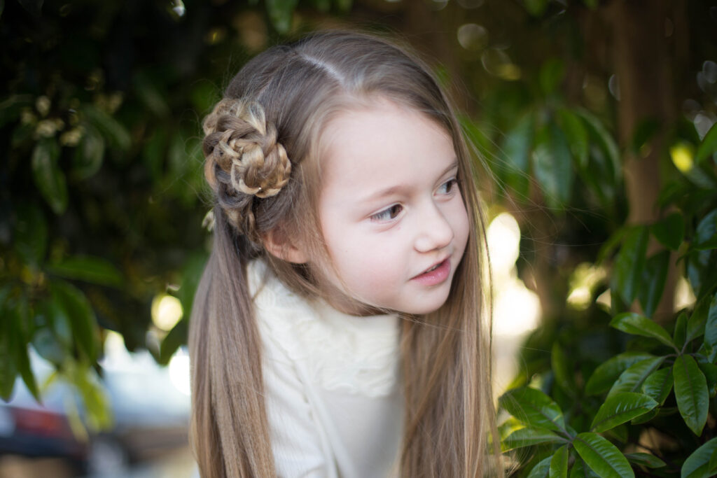 Young girl with a white shirt playing outside and modeling "Side Triple Flower" hairstyle