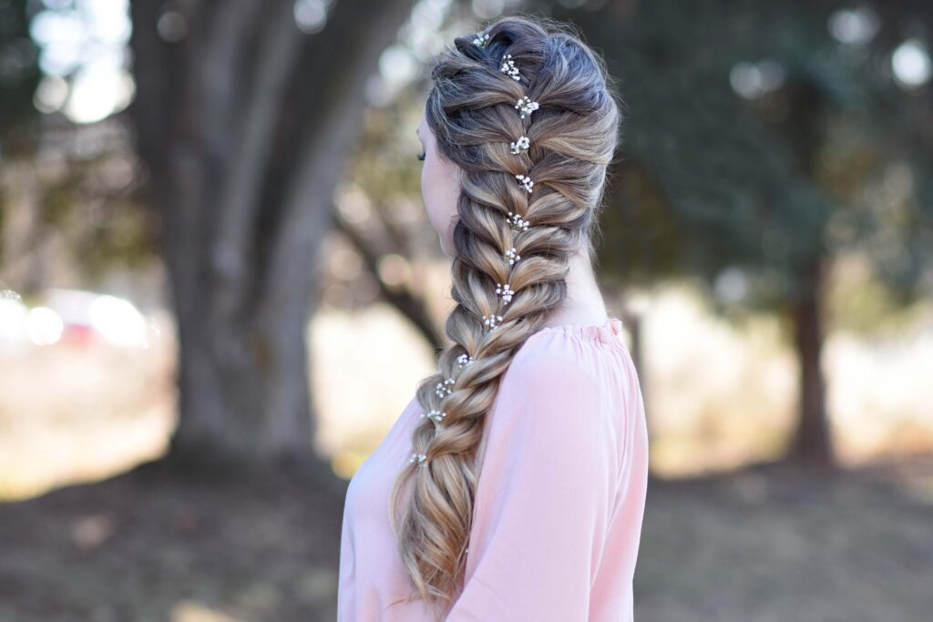 Side view of girl wearing a pink shirt standing outside modeling "Side Faux Braid" hairstyle