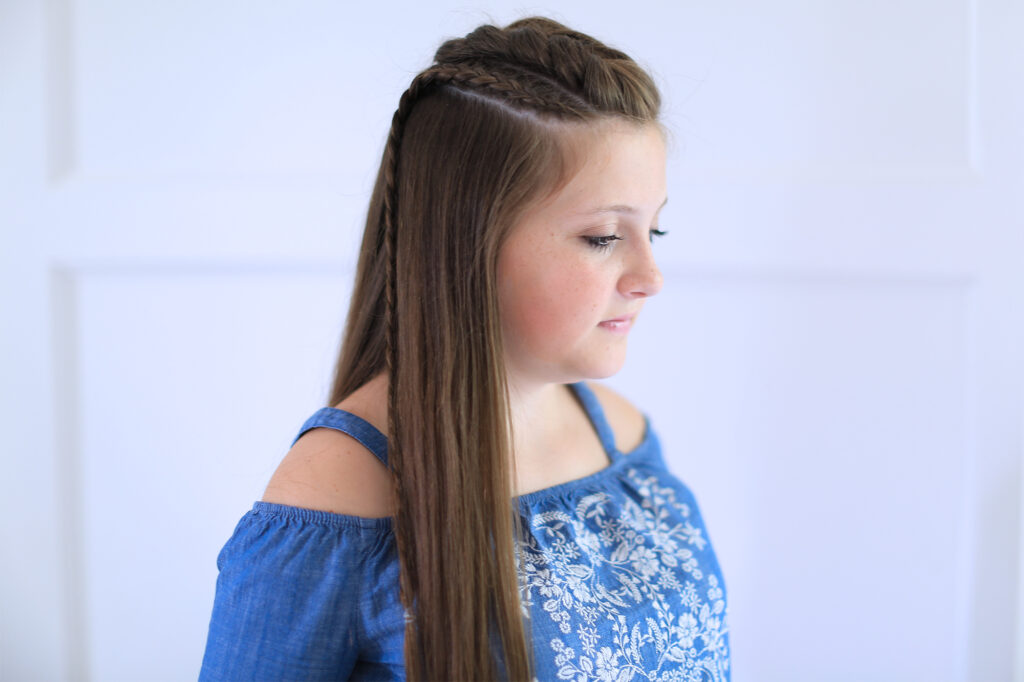 Side view of girl with blue shirt standing indoors modeling the "Dutch Lace Braid Combo" hairstyle