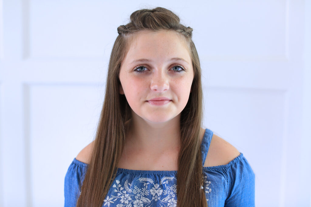 Girl standing indoors smiling modeling the "Dutch Lace Braid Combo" hairstyle