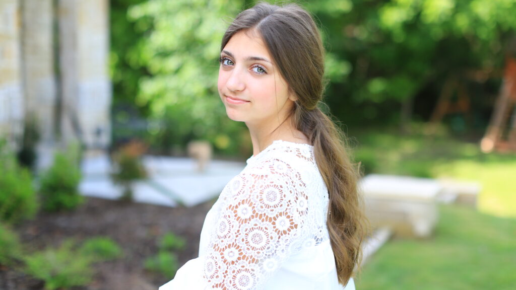 Profile view of young girl smiling and wearing a white shirt standing outside