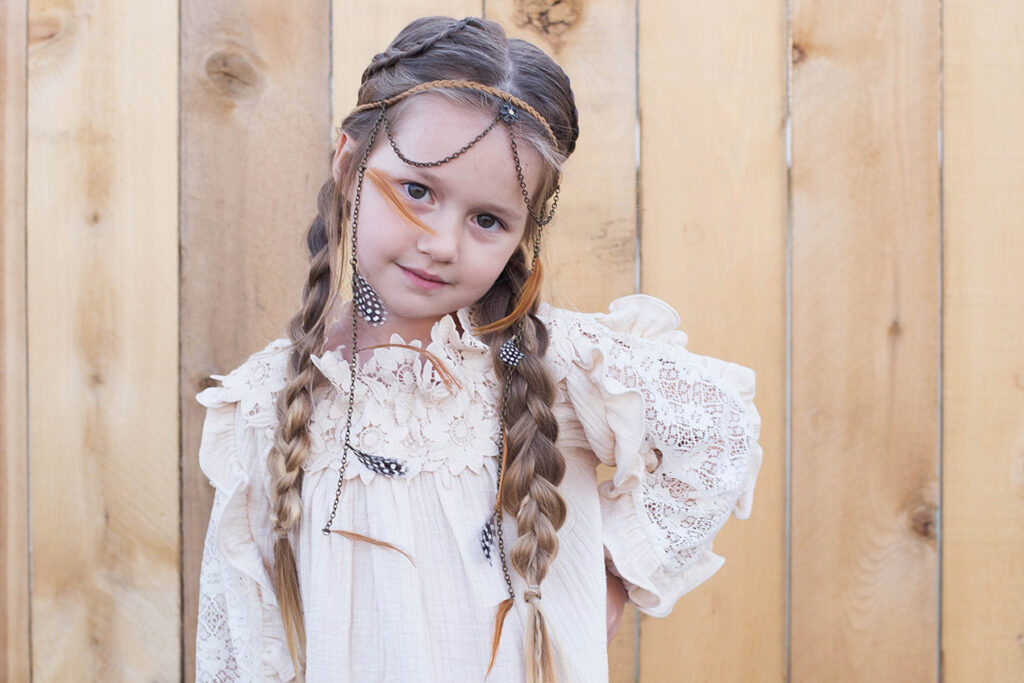 Girl with hands on her hips outside wearing a boho-inspired headband modeling "Boho Side Braids" hairstyle