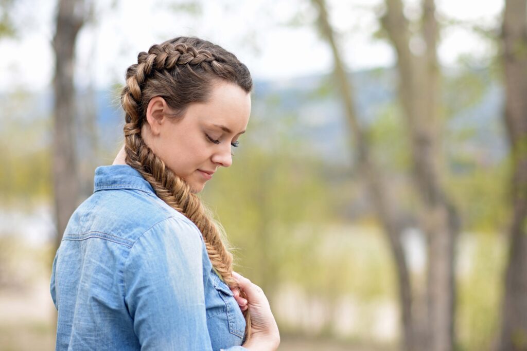 Side profile girl wearing a blue shirt standing outside modeling "Double Dutch Fishtails" hairstyle