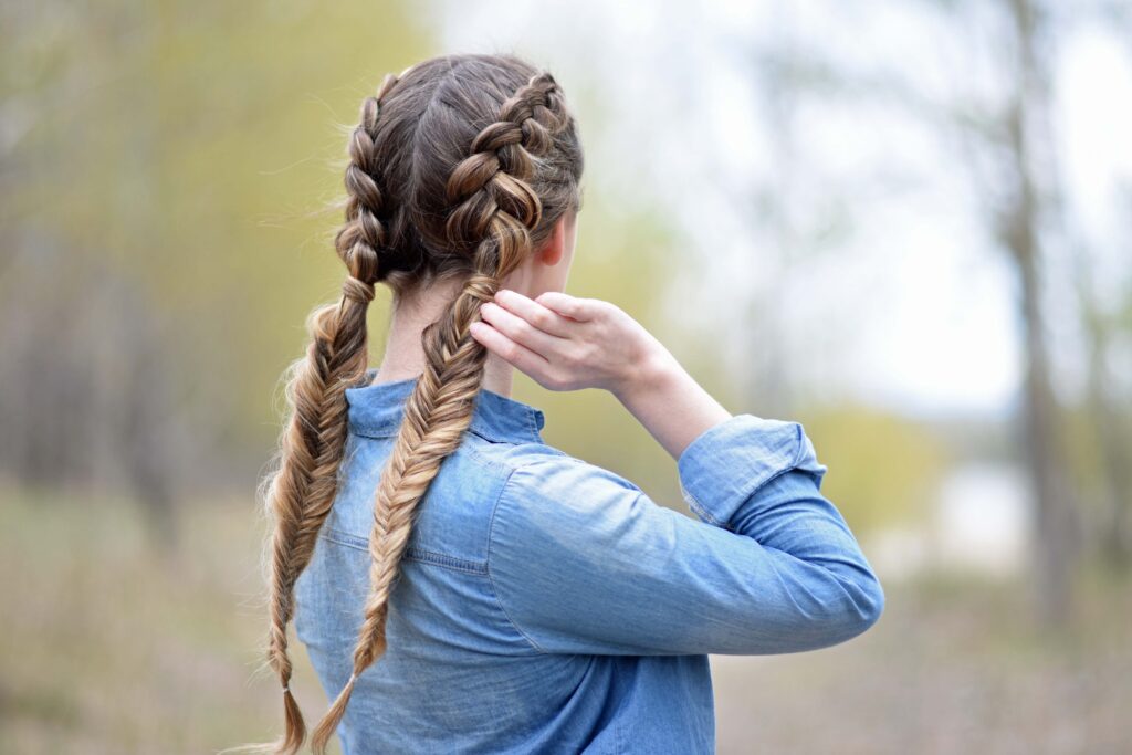 Back view of girl wearing a blue shirt standing outside modeling "Double Dutch Fishtails" hairstyle