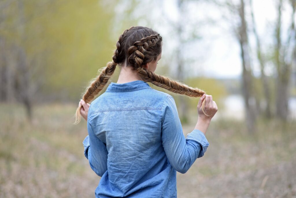 Back view of girl standing outside holding her hair modeling "Double Dutch Fishtails" hairstyle