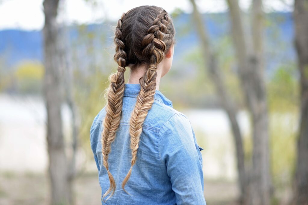 Back view of girl wearing a blue shirt standing outside modeling "Double Dutch Fishtails" hairstyle