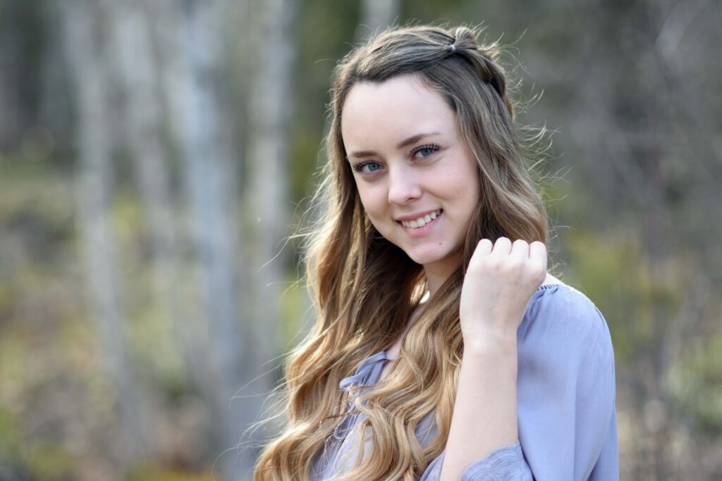 Portrait of a young girl with long hair smiling while standing in a wooded area 