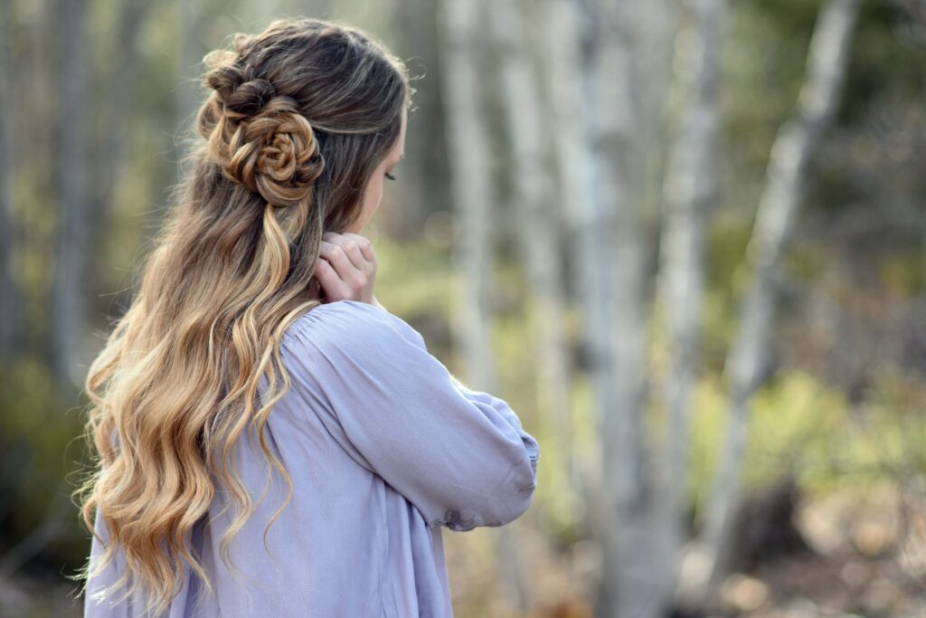 Side view of girl standing outside in the wooded area modeling the "Lace Pull-Thru Rosette Bun" hairstyle