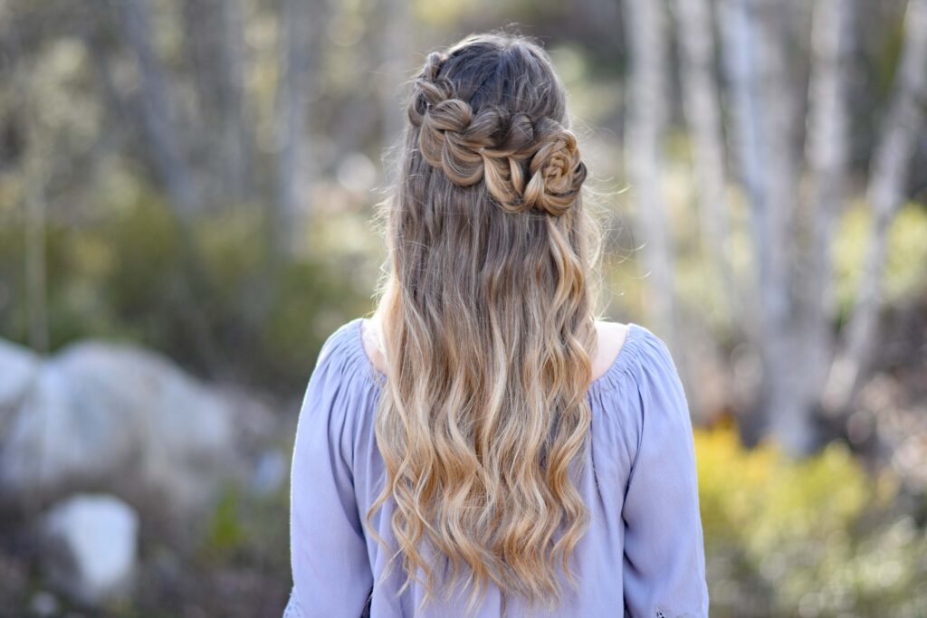 Back view of girl standing outside in the wooded area modeling the "Lace Pull-Thru Rosette Bun" hairstyle