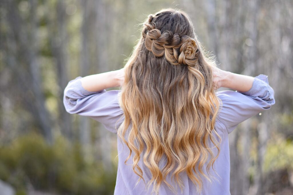 Back view of girl standing outside in the wooded area modeling the "Lace Pull-Thru Rosette Bun" hairstyle while holding her neck