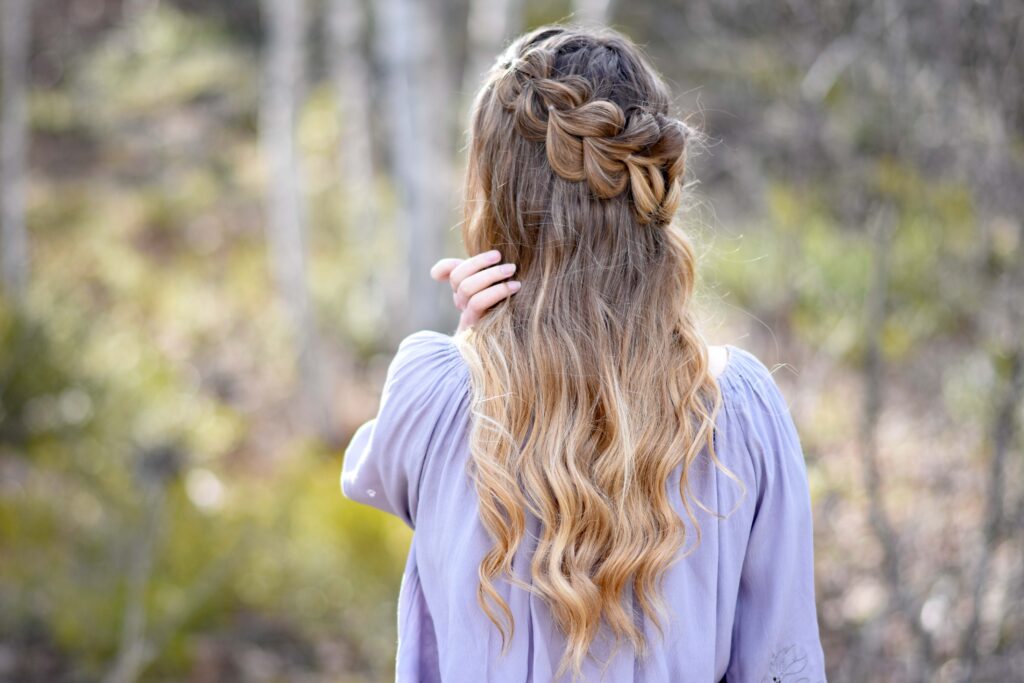 Back view of girl standing outside in the wooded area modeling the "Lace Pull-Thru Rosette Bun" hairstyle