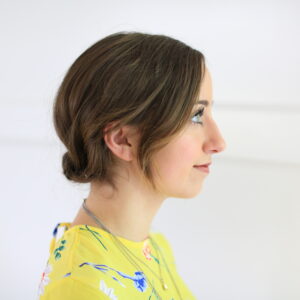 Side view of girl standing in front of white background with a yellow shirt modeling "Easy Rolled Updo" Hairstyle