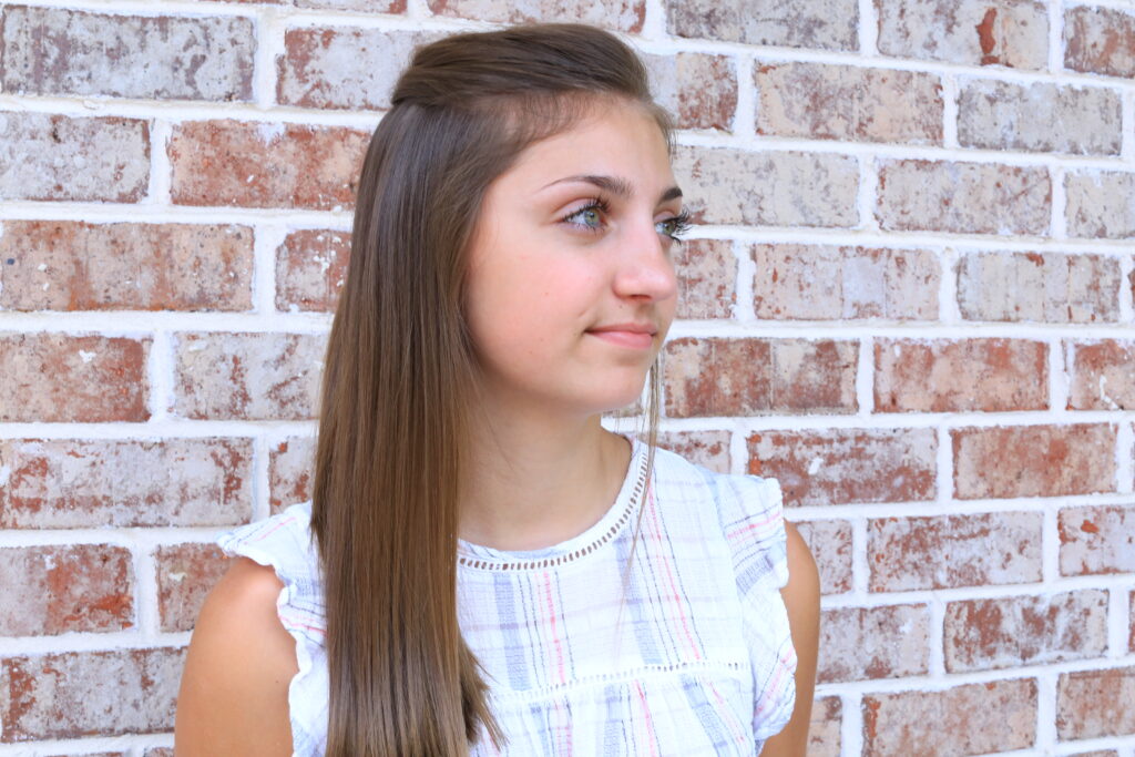 Young girl with long hair smiling while standing outside.